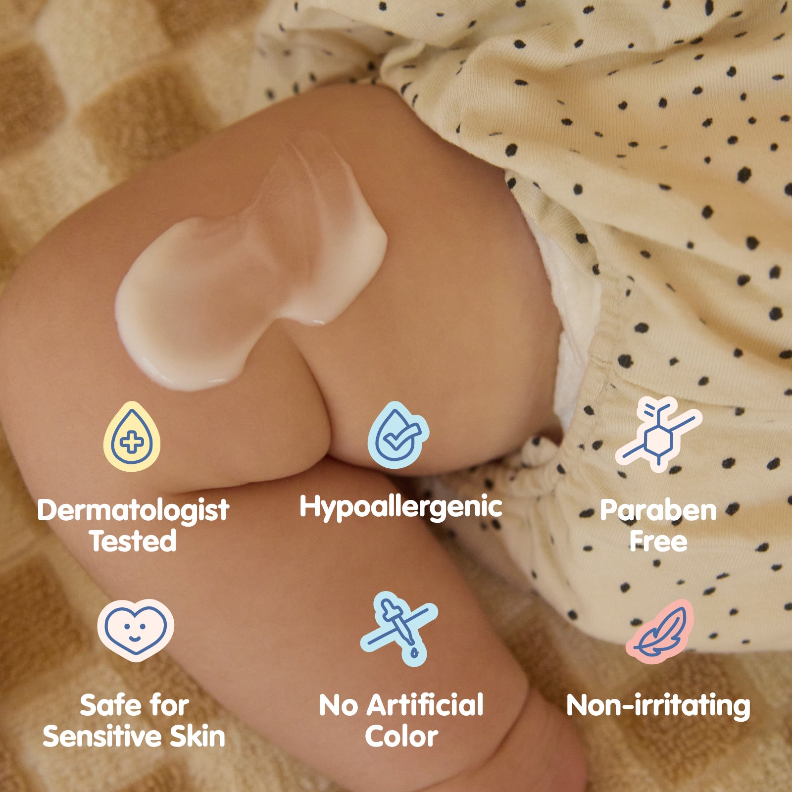 Close-up of a baby’s leg with a dollop of All Over ointment applied to the skin. The baby is wearing beige, polka-dotted shorts while lying on a soft, neutral-toned blanket. Overlaid icons and text highlight key product benefits, including 'Dermatologist Tested,' 'Hypoallergenic,' 'Paraben Free,' 'Safe for Sensitive Skin,' 'No Artificial Color,' and 'Non-irritating,' reinforcing the gentle and safe formulation of the skincare product.